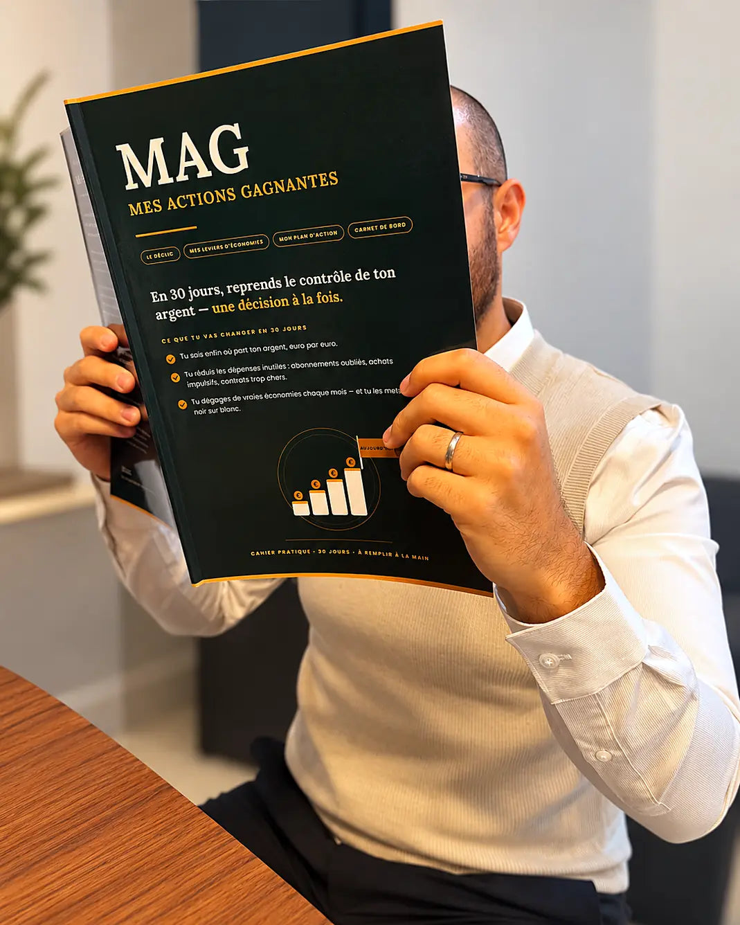 Le cahier MAG tenu en main, au bureau